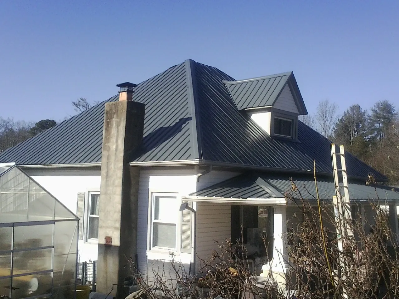 Dark blue standing seam metal roof on a white farmhouse with dormer — Slate & Tile Roof Repair by Roofing Brothers in Little Sioux