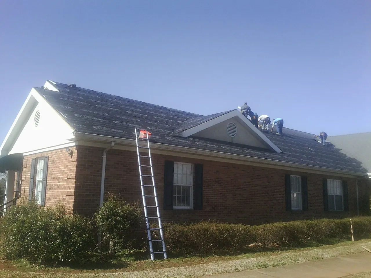 Crew tearing shingles off a brick ranch roof with a ladder set — Emergency Roof Repair work by our crew in Little Sioux