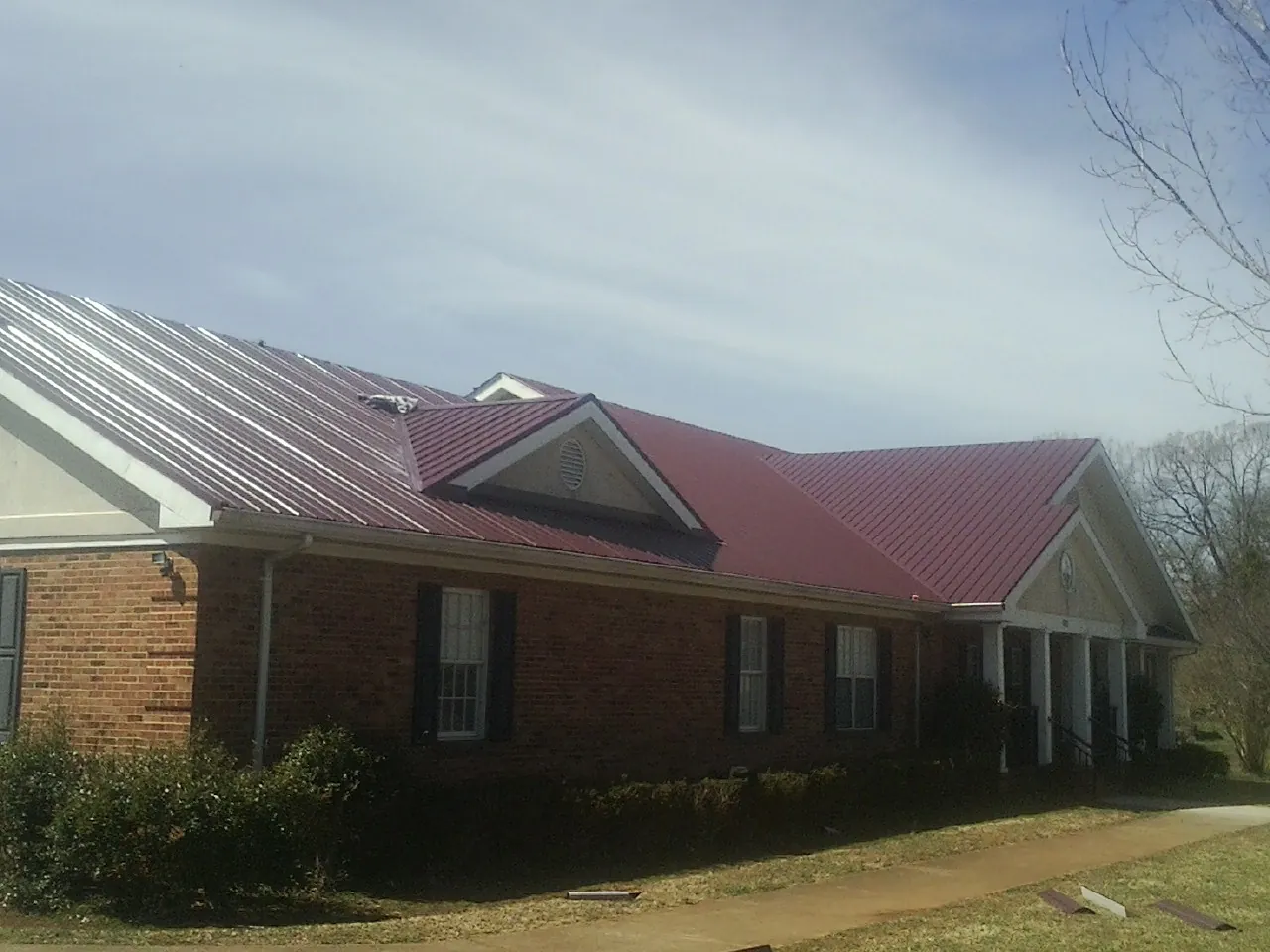Red metal roof with gabled entries on a long brick building, from a Hail Damage Roof Repair job in Little Sioux