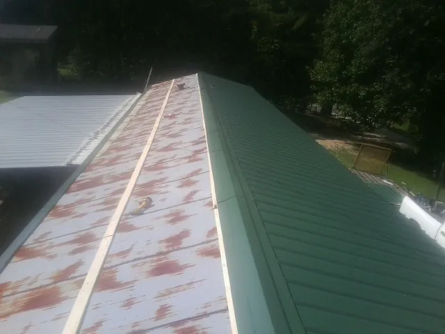 Old rusted panels beside newly installed green metal roofing — Wind Damage Roof Repair by Roofing Brothers in Little Sioux