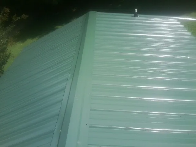 New green metal panels meeting at the ridge of a roof — Flat Roof Repair work by our crew in Little Sioux