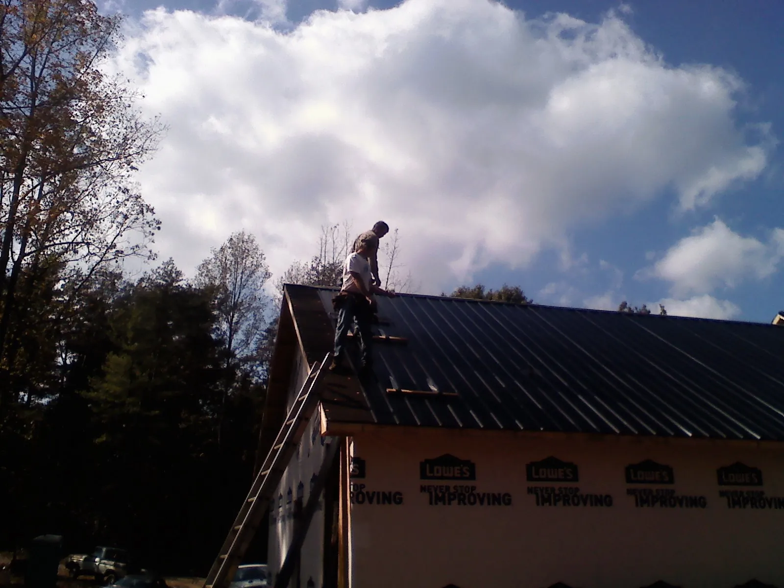 Roofer fastening dark metal panels high against a cloudy sky, from a Roof Inspection job in Little Sioux