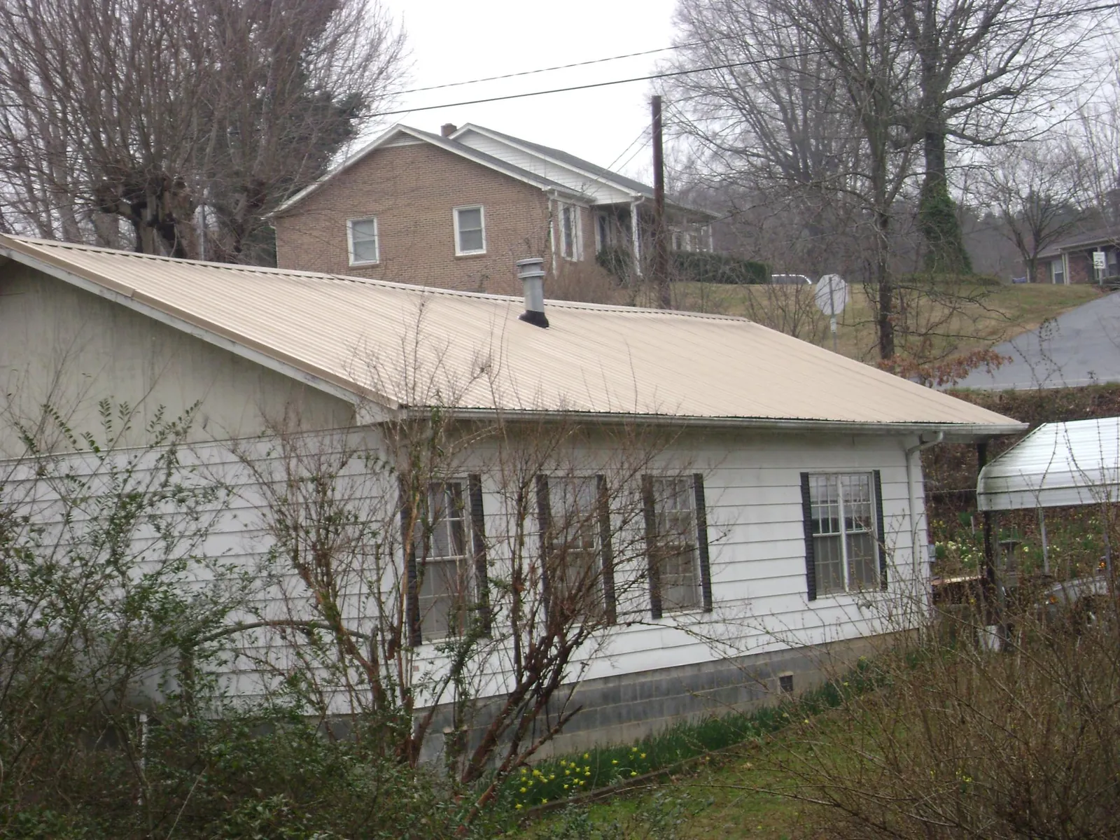 Tan metal roof on a white sided house set into a hillside — Commercial Roofing by Roofing Brothers in Little Sioux