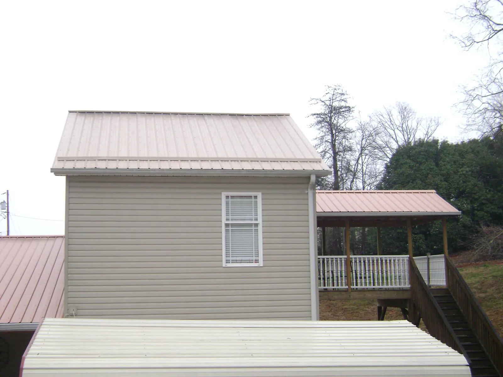 Tan metal roofs on a two story addition and attached porch, from a Roof Replacement job in Little Sioux